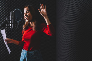 Pretty Asian female singer recording songs by using a studio microphone and pop shield on mic with passion in music recording studio. Performance and show in the music business. Image with copy space.